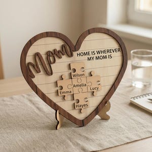May include: Wooden heart-shaped plaque with a dark brown border and the word "Mom" in cursive. The plaque features a puzzle design with the names "Wilson," "Emma," "Amelia," "Lucy," and "Hayes." The text "HOME IS WHEREVER MY MOM IS" is also included.