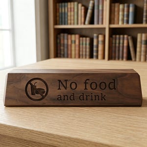 May include: A rectangular, wooden sign with the words "No food and drink" engraved in a serif font. The sign also features a circular icon depicting a crossed-out cup and sandwich. The sign is made of dark brown wood.