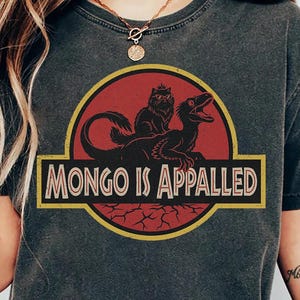 May include: Dark gray t-shirt featuring a humorous graphic. The design includes a red circle with a black silhouette of a creature and the text "MONGO IS APPALLED" in a yellow-bordered rectangle. The shirt is a casual wear item.