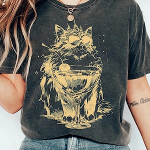 May include: Dark grey t-shirt with a yellow illustration of a cat wearing sunglasses and holding a cocktail with a cherry. The cat is sitting in front of the cocktail glass. The shirt has a vintage, worn appearance.