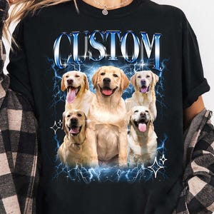 May include: Black long-sleeve t-shirt featuring a graphic of six golden retriever dogs with the word "CUSTOM" in blue, outlined in white. The dogs are surrounded by blue lightning bolts and stars.