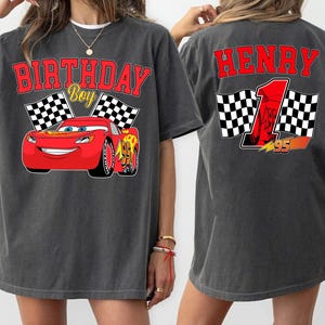 Pu&ograve; includere: T-shirt grigio scuro con un'auto da corsa rossa dei cartoni animati e la scritta "BIRTHDAY BOY". La parte posteriore della maglietta ha il nome "HENRY", il numero 1 e bandiere a scacchi. Il design &egrave; rosso e giallo.
