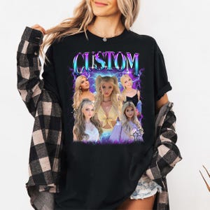 May include: Black long-sleeved t-shirt with a graphic design featuring the word "CUSTOM" in a stylized font. The design includes images of a person with blonde hair, set against a backdrop of purple and blue lightning bolts. The shirt is worn by a person.