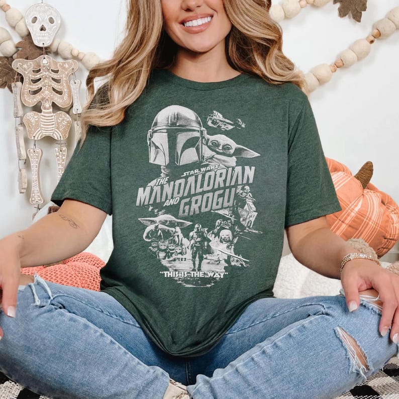 May include: Dark green t-shirt featuring a graphic of The Mandalorian and Grogu from Star Wars. The design includes images of the characters and the text "THE MANDALORIAN AND GROGU" and "THIS IS THE WAY" in white.