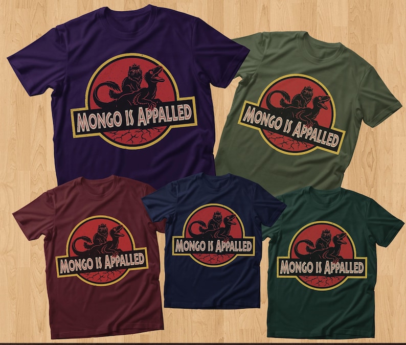 Peut inclure: Cinq t-shirts &agrave; manches courtes de diff&eacute;rentes couleurs : violet, vert olive, bordeaux, bleu marine et vert fonc&eacute;. Chaque chemise pr&eacute;sente un graphisme avec un dinosaure et le texte "MONGO IS APPALLED" dans un design jaune et rouge.