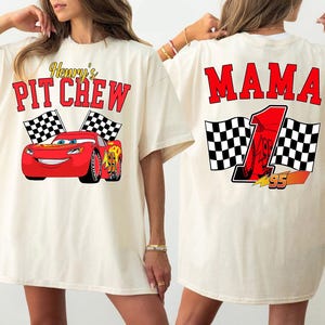 Pu&ograve; includere: T-shirt color crema con grafica di auto da corsa rossa e la scritta "Henry's Pit Crew" sul davanti. Il retro della maglietta mostra la parola "MAMA" e un numero di gara.