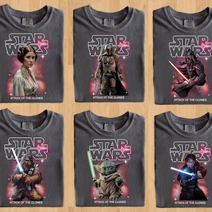 May include: Six gray t-shirts featuring Star Wars characters. Each shirt displays the Star Wars logo and the text "ATTACK OF THE CLONES." The shirts showcase characters like Princess Leia, Boba Fett, Darth Vader, Chewbacca, Yoda, and Anakin Skywalker, each with a unique design.