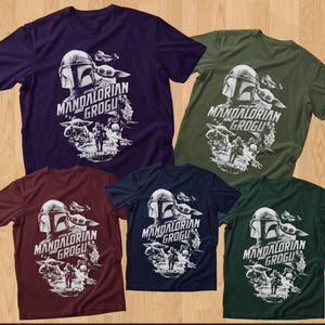 May include: Five short-sleeved t-shirts in various colors: purple, olive green, burgundy, navy blue, and dark green. Each shirt features a white graphic of The Mandalorian and Grogu, with the text "THE MANDALORIAN AND GROGU" and "THIS IS THE WAY".