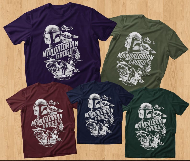 May include: Five short-sleeved t-shirts in various colors: purple, olive green, burgundy, navy blue, and dark green. Each shirt features a white graphic of The Mandalorian and Grogu, with the text "THE MANDALORIAN AND GROGU" and "THIS IS THE WAY".