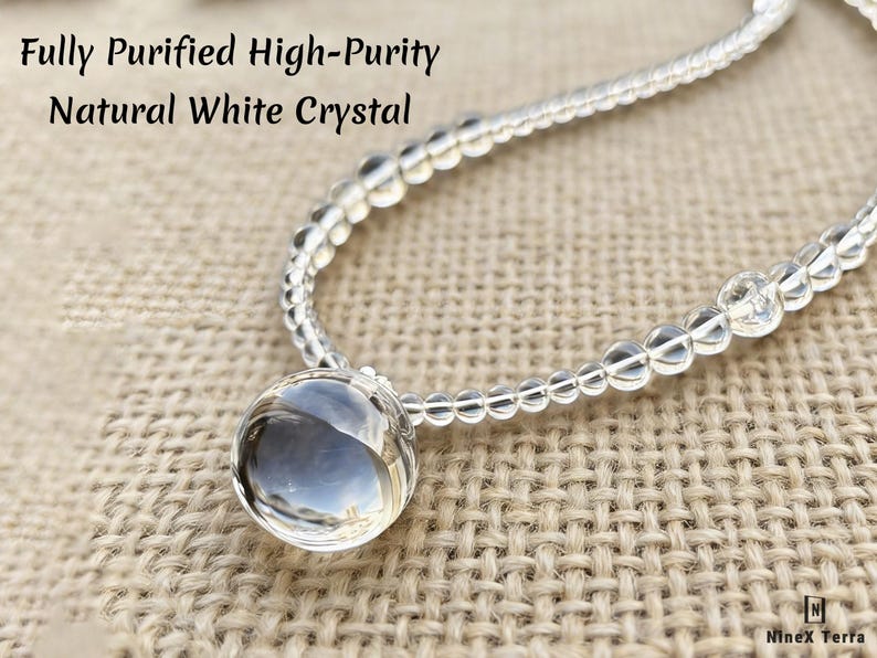 May include: A clear, natural white crystal necklace with a large, round pendant. The necklace is made of small, clear beads and is displayed on a textured, tan surface. Text on the image reads: "Fully Purified High-Purity Natural White Crystal."