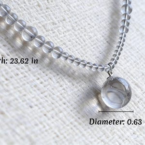 May include: A clear quartz necklace with a round pendant. The necklace is 23.62 inches long, and the pendant has a diameter of 0.63 inches. The necklace is made of small, clear beads.