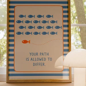 Può includere: Stampa artistica incorniciata con un messaggio motivazionale. La stampa presenta pesci blu che nuotano in una direzione, con un pesce arancione che nuota nella direzione opposta. Il testo recita: "YOUR PATH IS ALLOWED TO DIFFER."