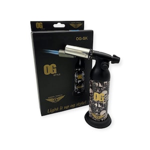 May include: Black and silver OG-SK torch lighter with a skull pattern. The lighter is on a black base, with a blue flame. The box behind the lighter has the text "OG STYLE" and "Light it up og style!"