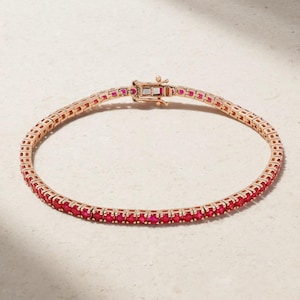 May include: A rose gold tennis bracelet with a row of vibrant red gemstones. The bracelet has a secure clasp and is designed with a delicate, elegant aesthetic. The gemstones are evenly spaced, creating a continuous line of colour.