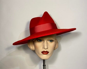 Puede incluir: Un sombrero rojo de ala ancha con una cinta de satén. El sombrero está en una cabeza de maniquí.