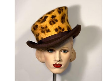 Puede incluir: Un sombrero de copa marrón con una corona de estampado de leopardo. El sombrero está en una cabeza de maniquí.