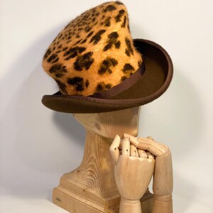 May include: A brown top hat with a leopard print crown. The hat is sitting on a wooden mannequin head.