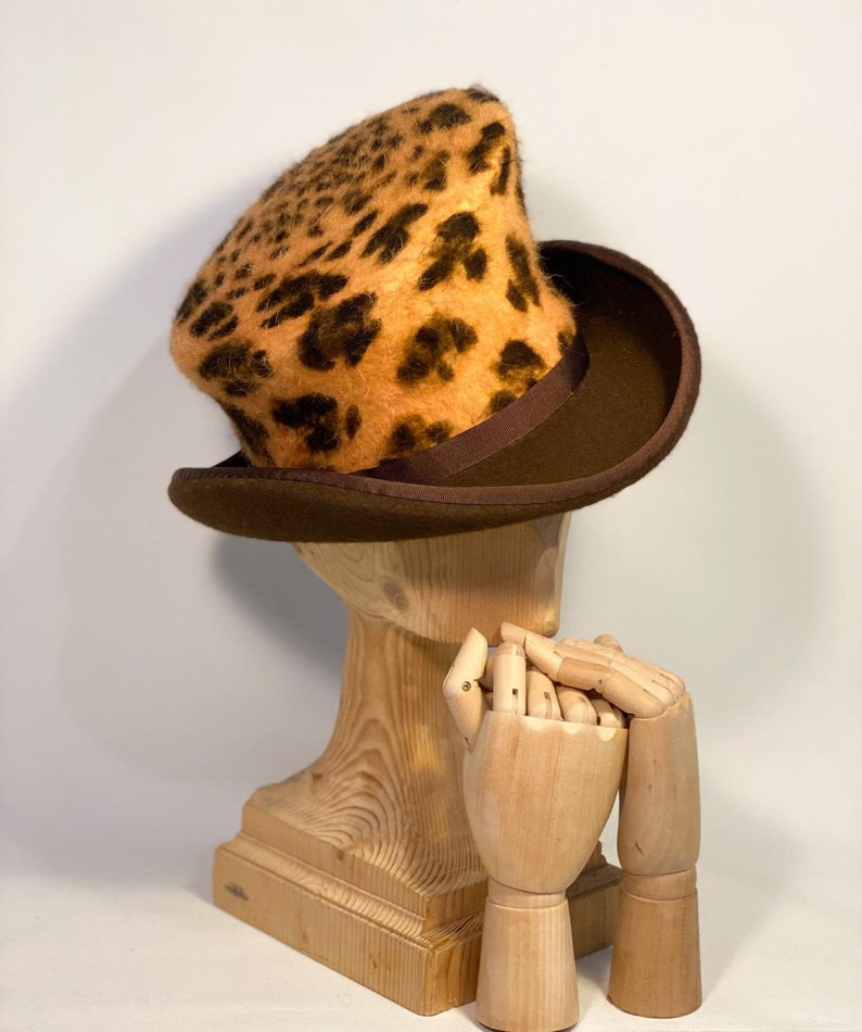 May include: A brown top hat with a leopard print crown. The hat is sitting on a wooden mannequin head.