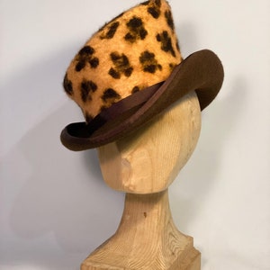 May include: A brown top hat with a leopard print crown. The hat is on a wooden hat stand.