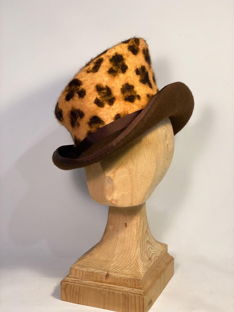 May include: A brown top hat with a leopard print crown. The hat is on a wooden hat stand.