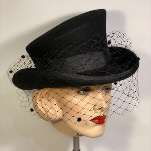 May include: A black top hat with a black veil and black bead accents. The hat is angled on a mannequin head.