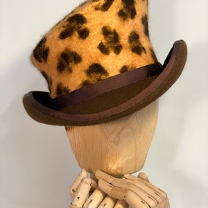 May include: A brown and tan top hat with a leopard print design. The hat has a brown ribbon around the base.