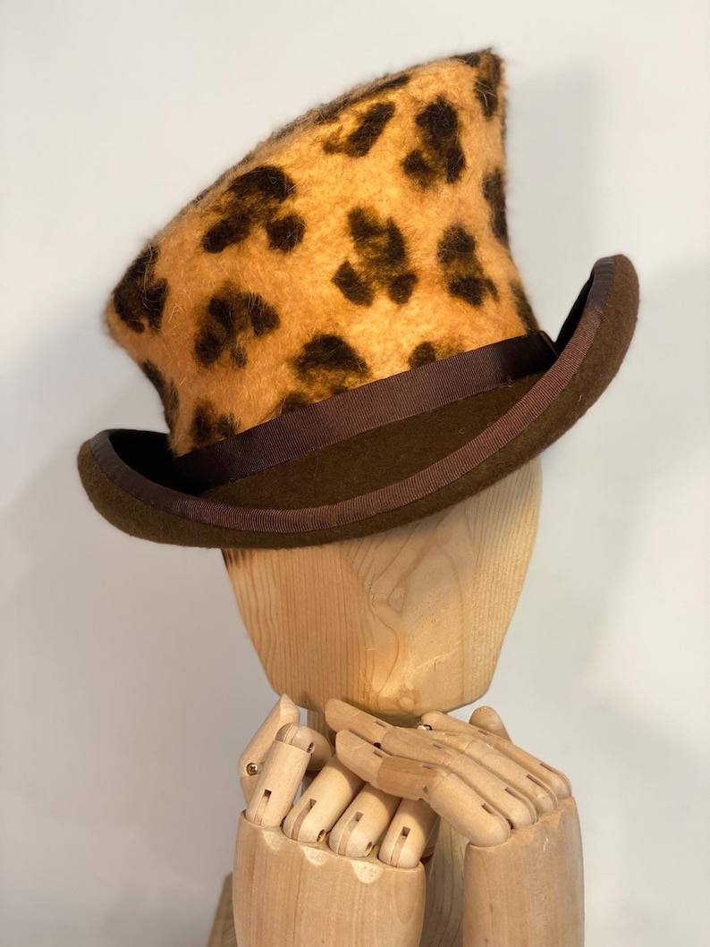 May include: A brown and tan top hat with a leopard print design. The hat has a brown ribbon around the base.