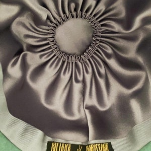 May include: The inside of a teal green felt hat with a gray satin lining and a gray grosgrain ribbon. The ribbon has a gold label with the text "Billini Borse" and a small whale graphic.