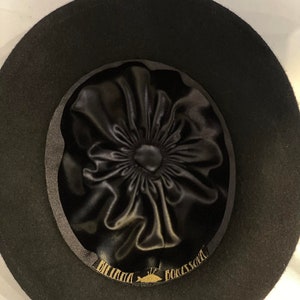 Puede incluir: Sombrero fedora de fieltro negro con forro de sat&eacute;n negro y una etiqueta dorada que dice "DORSAY" y "BILLINI" dentro del sombrero.