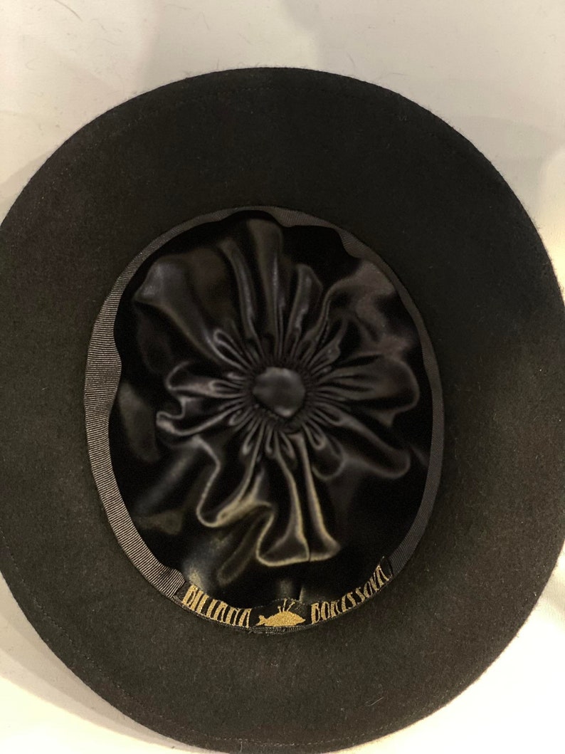 Puede incluir: Sombrero fedora de fieltro negro con forro de sat&eacute;n negro y una etiqueta dorada que dice "DORSAY" y "BILLINI" dentro del sombrero.