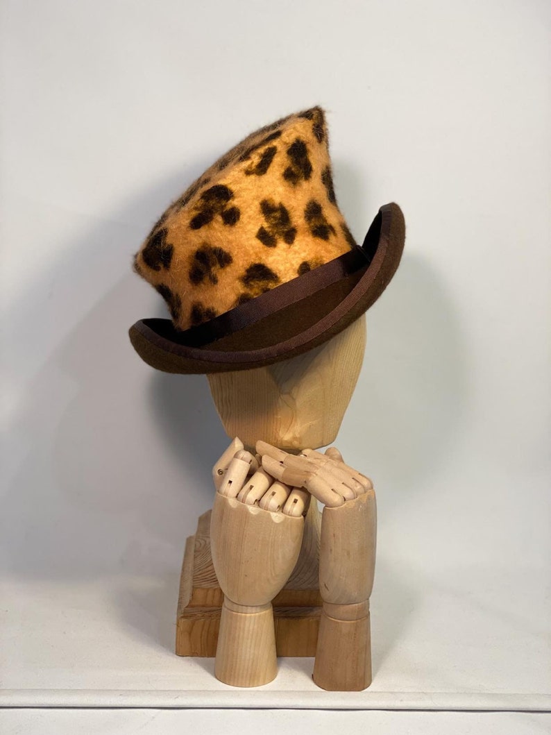 May include: A brown and tan leopard print top hat with a brown brim. The hat is sitting on a wooden mannequin head.