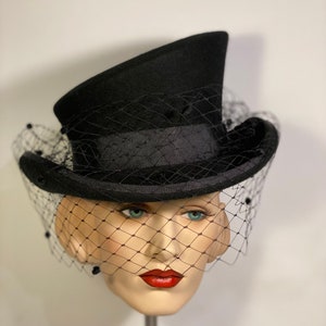 May include: A black top hat with a black veil. The hat has a wide brim and a tall crown. The veil is made of a fine mesh and is attached to the hat with a black ribbon.