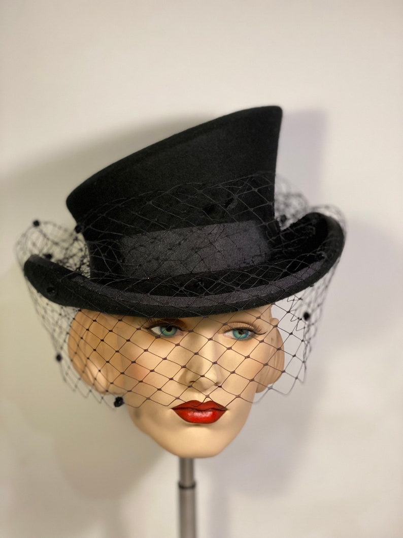 May include: A black top hat with a black veil. The hat has a wide brim and a tall crown. The veil is made of a fine mesh and is attached to the hat with a black ribbon.