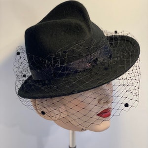 Puede incluir: Un sombrero de fieltro negro con ala ancha y velo negro. El sombrero tiene una forma &uacute;nica y est&aacute; decorado con peque&ntilde;os puntos negros.
