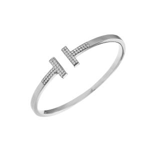 May include: A silver-toned open cuff bracelet featuring two T-shaped ends. Each T-shaped terminal is embellished with a pavé setting of small, clear, round-cut stones that catch the light, contrasting with the smooth, polished metal band.