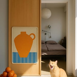 May include: A room interior with a wooden sliding door featuring a framed artwork with an orange vase design above blue stripes. A bowl of oranges sits on a table. An orange cat yawns in the sunlight.
