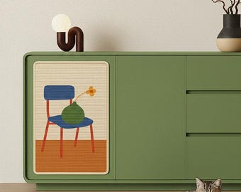 May include: A green cabinet with a decorative panel featuring a chair, vase, and flower illustration. A brown and white lamp sits on top. A tabby cat rests on a patterned rug in front of the cabinet.