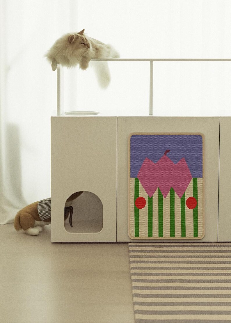 May include: A modern cat furniture set with a beige cabinet, a decorative mat with a geometric design, and a fluffy cat resting on top. The mat features a pink and green pattern. A dog is partially visible inside the cabinet.