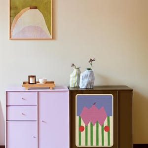 May include: A modern interior scene featuring a lilac cabinet with drawers and a brown cabinet with a colorful graphic. A framed abstract painting hangs above the cabinets. Decorative vases and a tray with a candle and bowl are on the lilac cabinet.