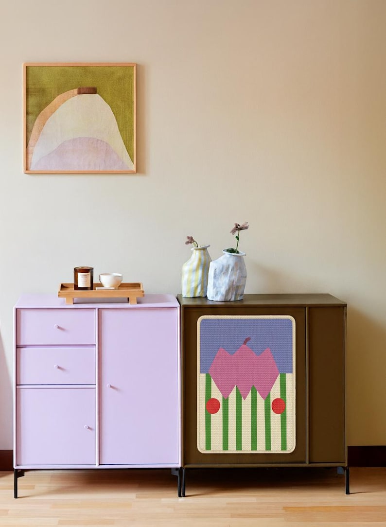 May include: A modern interior scene featuring a lilac cabinet with drawers and a brown cabinet with a colorful graphic. A framed abstract painting hangs above the cabinets. Decorative vases and a tray with a candle and bowl are on the lilac cabinet.