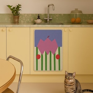 May include: A kitchen scene featuring a decorative mat with a pink and green design, set against yellow cabinets and a light green countertop. A tabby cat sits in the foreground.