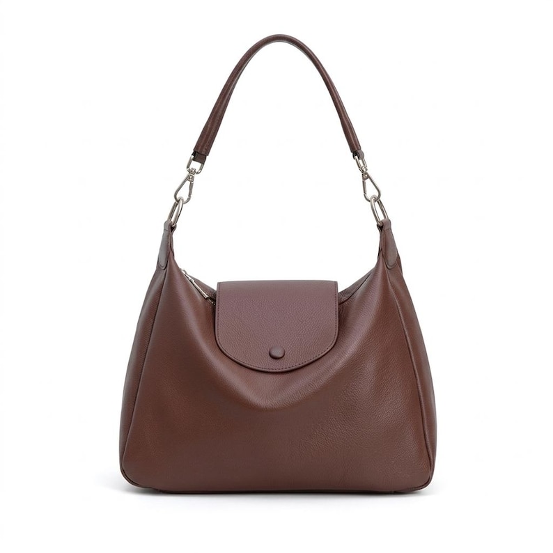 May include: A brown leather shoulder bag with a curved shape and a flap closure. The bag has a single shoulder strap and silver-tone hardware. The bag is made of a smooth, matte leather.