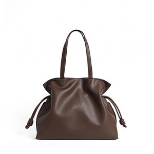 May include: A dark brown tote bag with a smooth finish, featuring two vertical shoulder straps and a drawstring closure on each side. The bag has a soft, gathered silhouette with knotted ends on the drawstrings, creating a structured yet flexible shape.