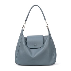 May include: A blue-grey leather shoulder bag with a flap closure and a single handle. The bag has silver-toned hardware and a rounded shape. The bag is approximately 35 cm wide and 30 cm tall.