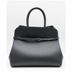 May include: A black tote bag with a structured design. The bag has a top handle and a thin strap with a buckle. The bag's shape is trapezoidal, with a wider base and a narrower top.