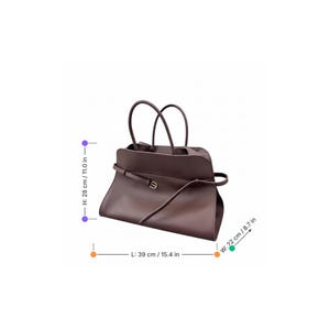 May include: A brown leather handbag with two top handles and a shoulder strap. The bag is 28 cm high, 39 cm long, and 22 cm wide. It features a belt detail with a gold-coloured buckle.