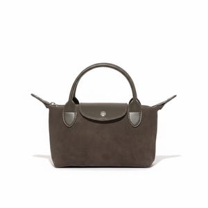 Puede incluir: Un bolso pequeño, marrón, con asa superior y cierre de solapa. El bolso tiene forma rectangular con cremallera a cada lado. El asa y la solapa son de un tono marrón más oscuro. El bolso está sobre un fondo blanco.