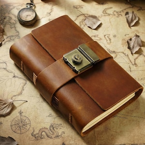 May include: A brown leather journal with a clasp closure. The journal is closed with a strap and a metal clasp. The journal is on a map with dried leaves and a pocket watch.