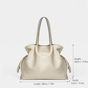 May include: A beige tote bag with two top handles and side drawstring details featuring knotted ends. The bag measures 38 cm or 15 inches in length, 30 cm or 11.8 inches in height, and 14 cm or 5.5 inches in depth as indicated by the text.