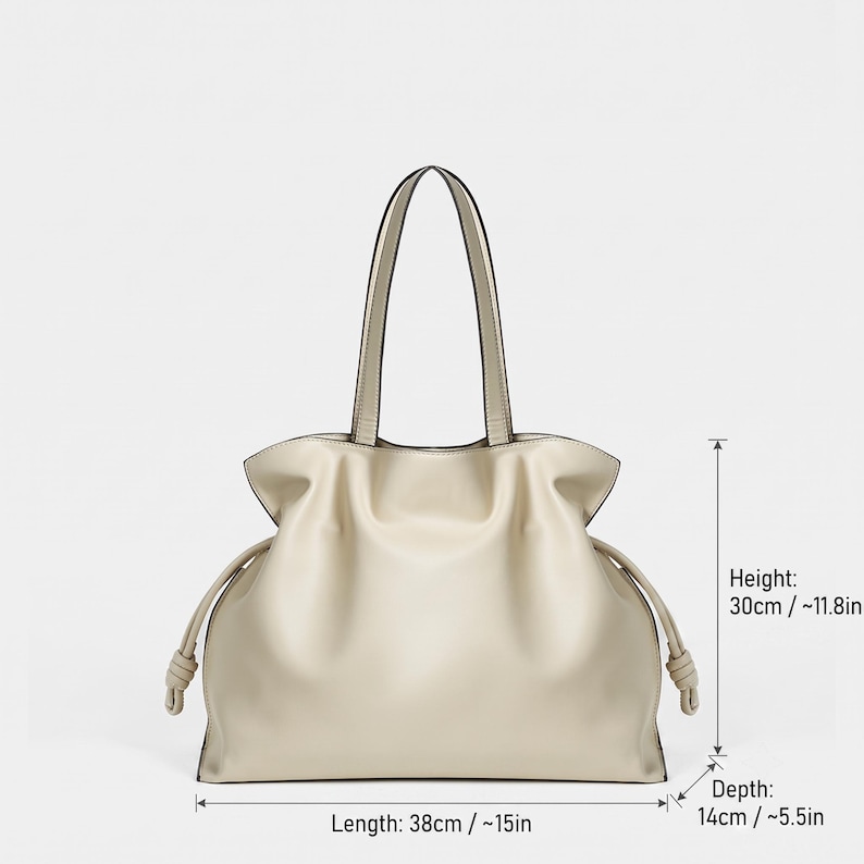 May include: A beige tote bag with two top handles and side drawstring details featuring knotted ends. The bag measures 38 cm or 15 inches in length, 30 cm or 11.8 inches in height, and 14 cm or 5.5 inches in depth as indicated by the text.